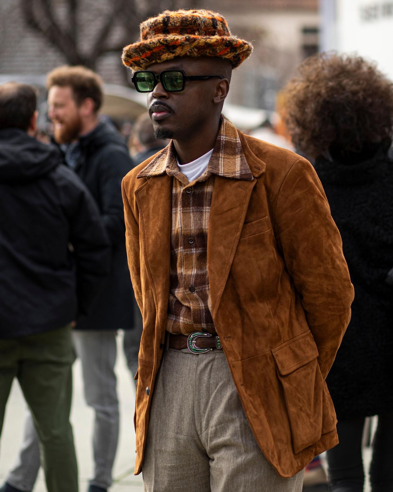 A man in a brown jacket and hat standing on a street