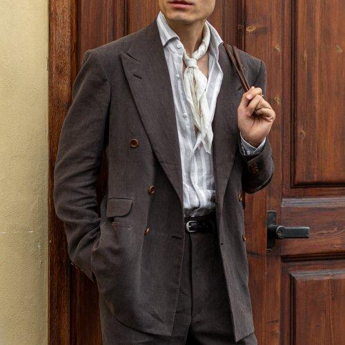 A man wearing a tailored coat layered over a grey striped shirt, paired with black pants