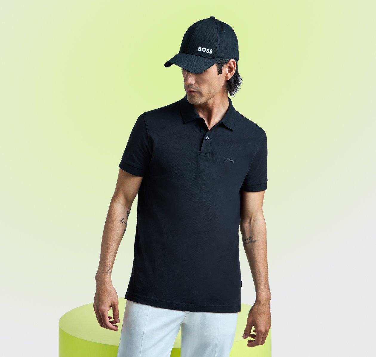 model wearing a black Hugo Boss men's polo shirt paired with light-colored trousers and a matching cap