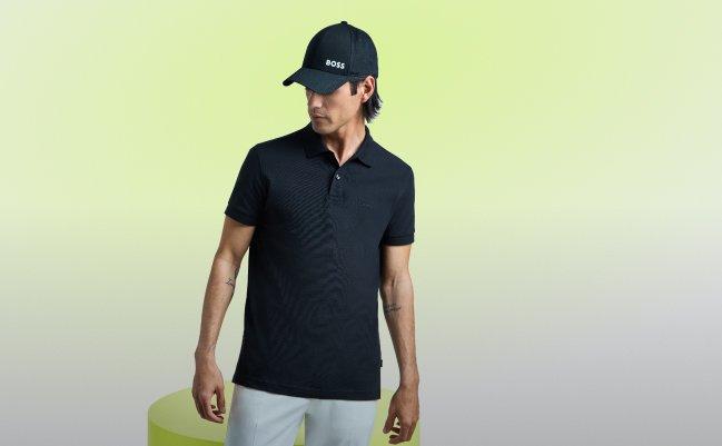 model wearing a black Hugo Boss men's polo shirt paired with light-colored trousers and a matching cap