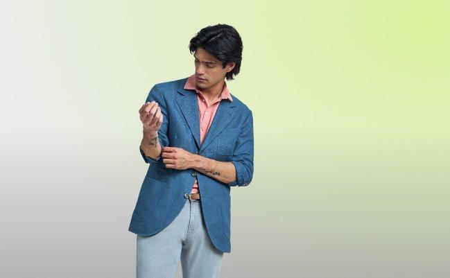 A man wearing a dark blue sport jacket with peach shirt and light blue jeans