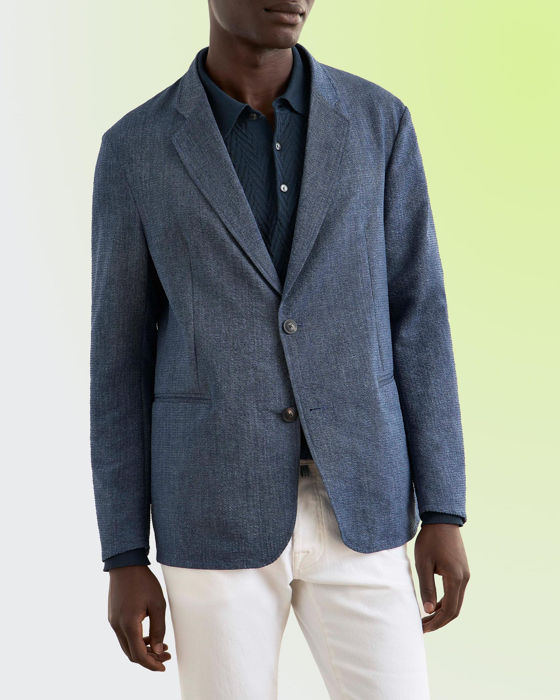 A man wearing a textured blue blazer paired with a dark button-up shirt and white trousers