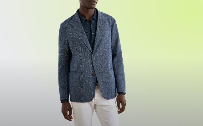 A man wearing a textured blue blazer paired with a dark button-up shirt and white trousers