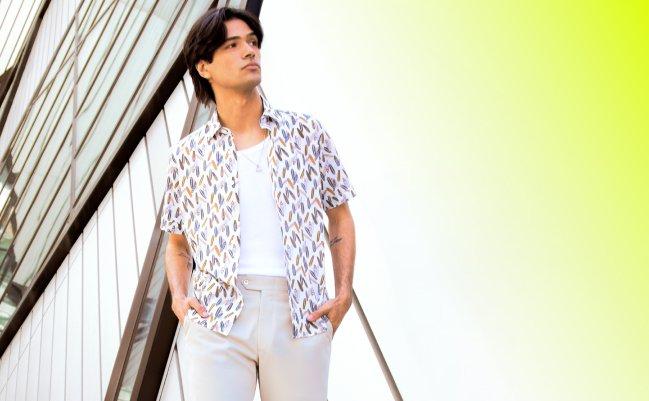 A man wearing a white short-sleeve patterned shirt paired with beige trousers and a white T-shirt underneath