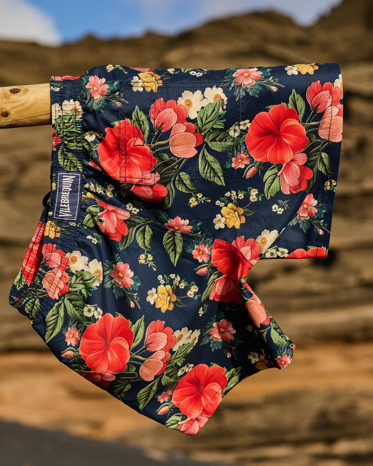 A men's swim shorts featuring a bold Hawaiian floral print on a dark navy background
