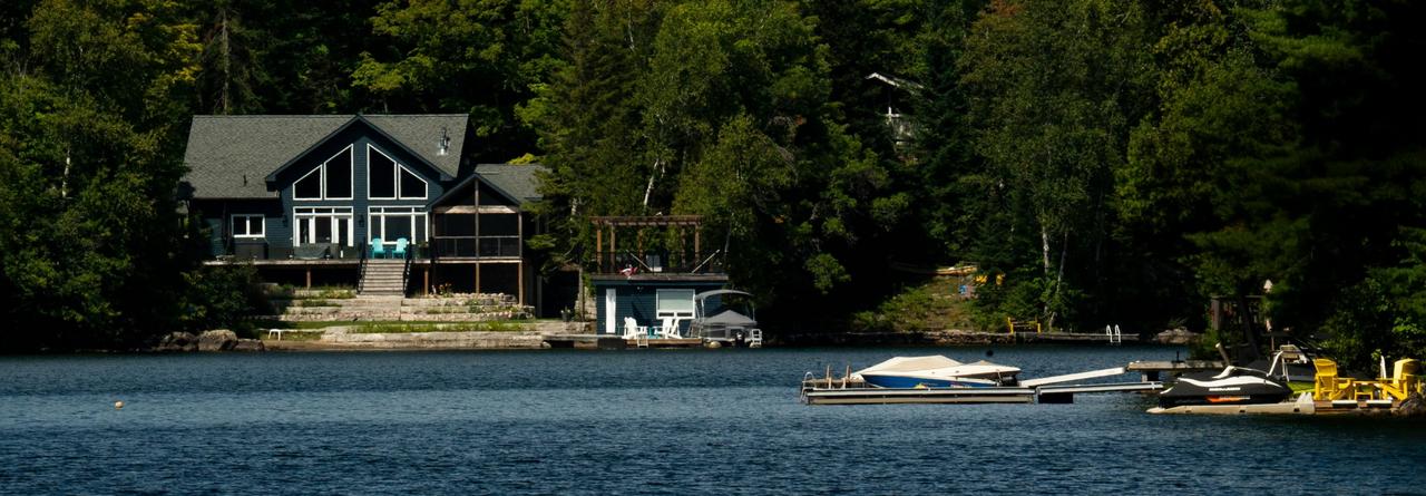 Une maison au bord d'un lac avec un bateau à moteur amarré au quai, entourée d'une forêt dense le long de la rive