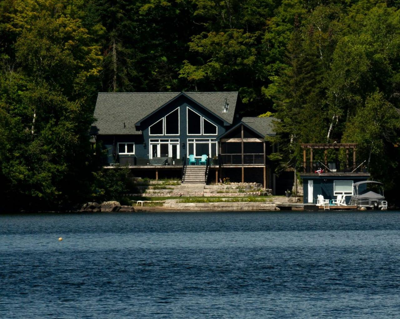 A lakeside home with a docked motorboat, surrounded by dense forest along the shoreline