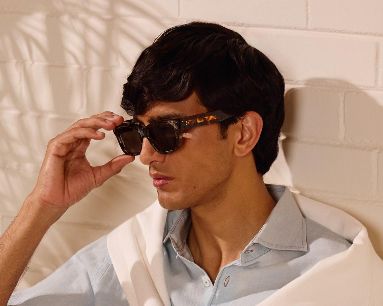  A man wearing a light blue collared shirt with black sunglasses