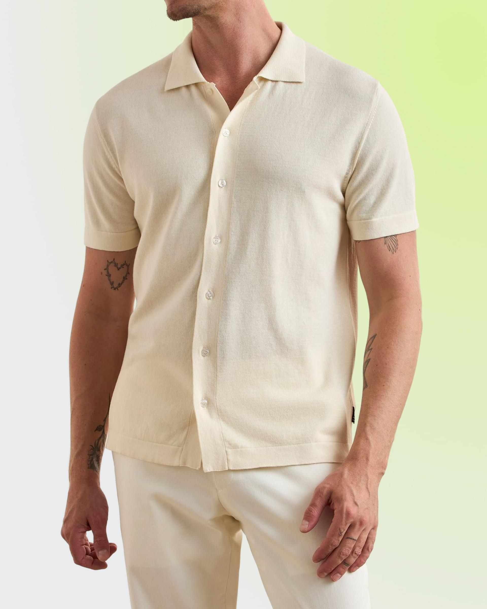 A man wearing a cream-colored short-sleeve button-down knit shirt paired with light-colored trousers
