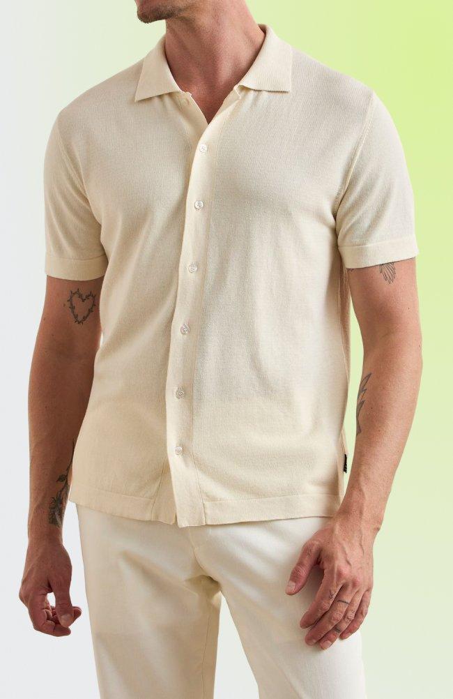 A man wearing a cream-colored short-sleeve button-down knit shirt paired with light-colored trousers