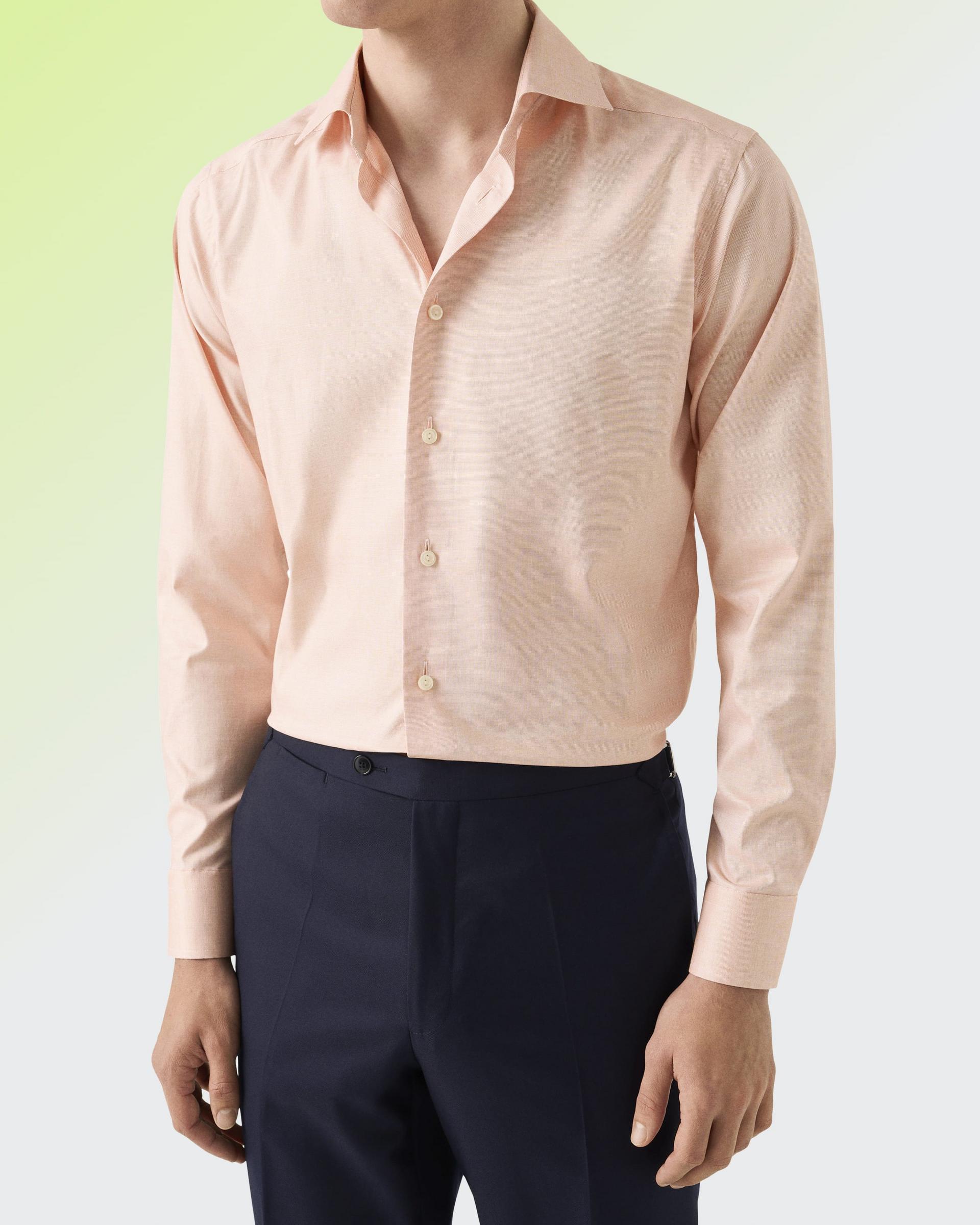 Un homme portant un vêtement rose pâle, accompagné d’un pantalon bleu marine foncé