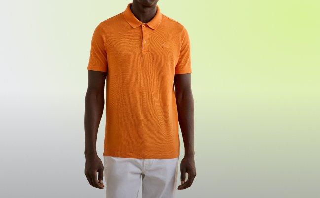 mannequin portant un polo orange vif associé à un pantalon blanc