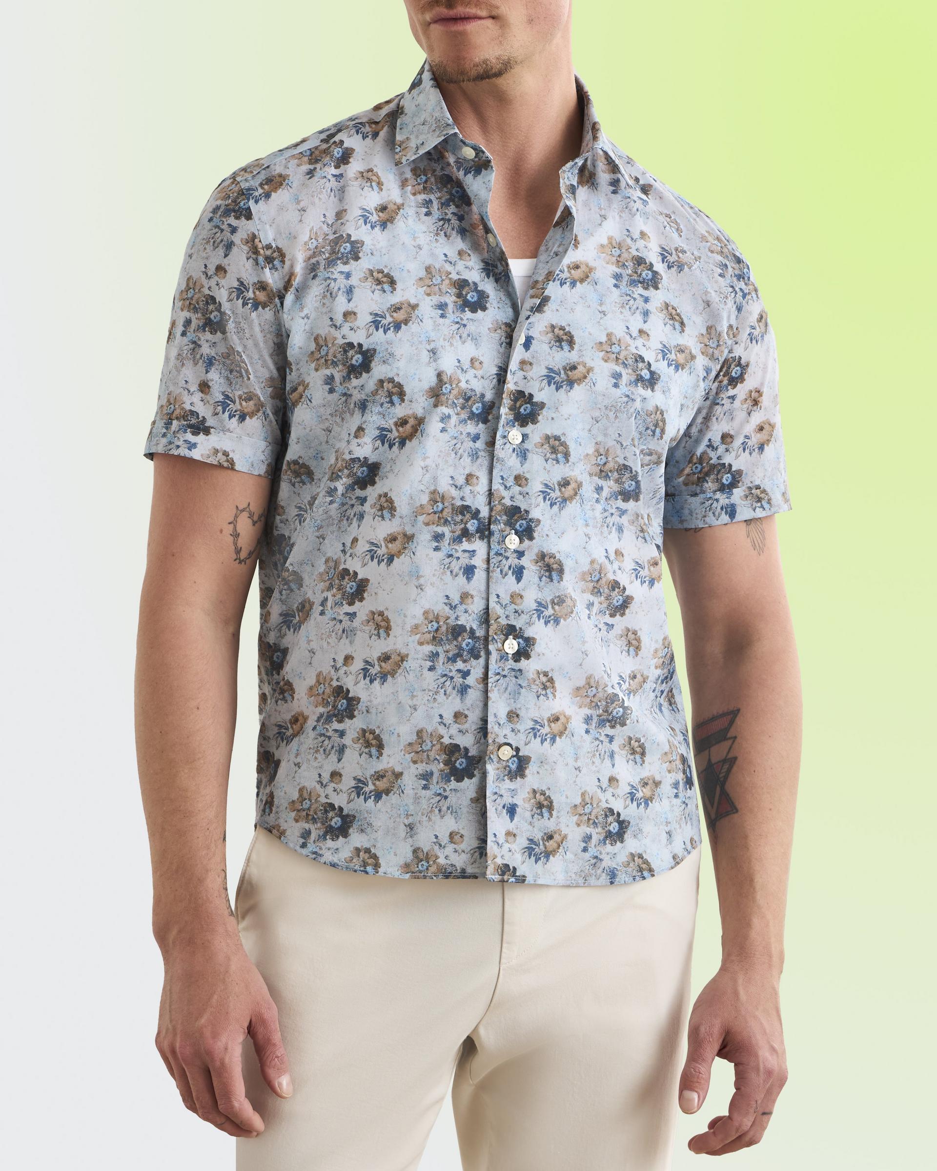 model wearing a light blue short-sleeve button-up shirt with a brown and blue floral pattern, paired with light beige pants
