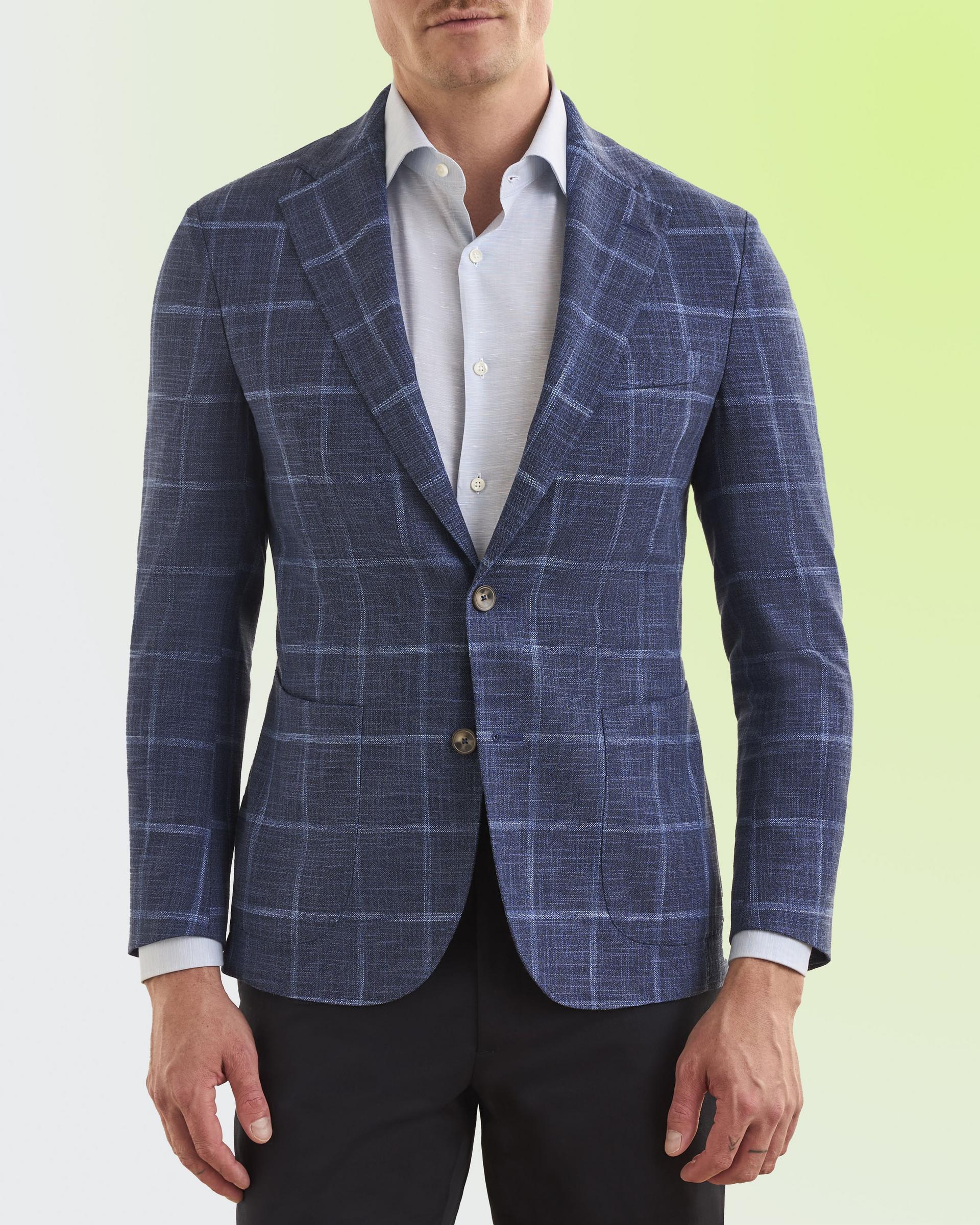 Model wearing a tailored blue plaid sport jacket with a subtle check pattern, paired with a light blue dress shirt and dark trousers