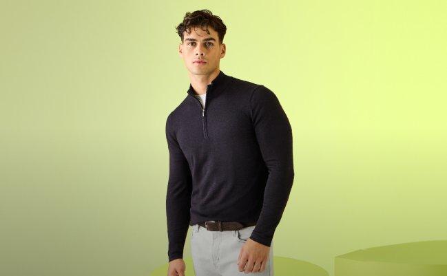 A male model wearing a black knit quarter zip sweater styled with white pants