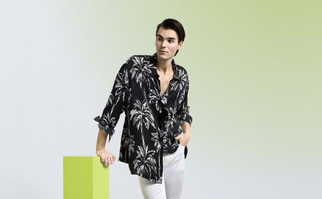 Homme portant une chemise décontractée noir et blanc à imprimé de feuilles de palmier, agencée à un pantalon blanc