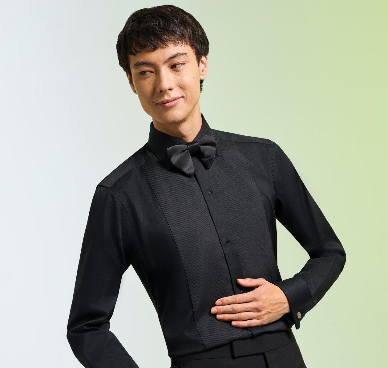 A male model wearing a black dress shirt, styled with a black bow tie and dress pants