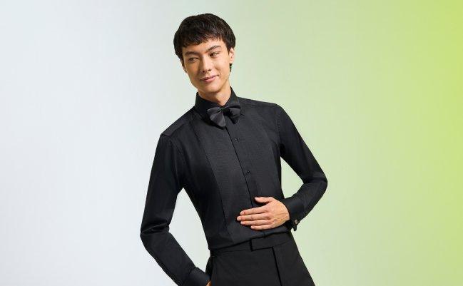A male model wearing a black dress shirt, styled with a black bow tie and dress pants