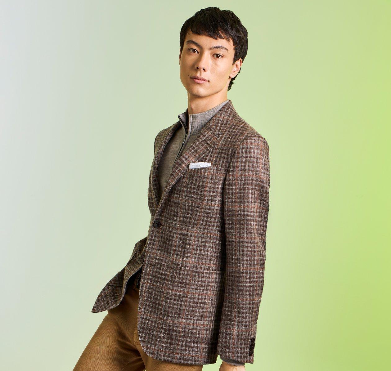 A man wearing a beige plaid sports jacket layered over a light sweater
