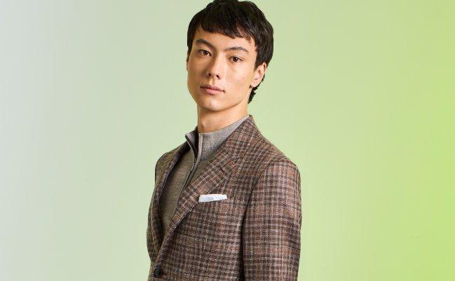 A man wearing a beige plaid sports jacket layered over a light sweater