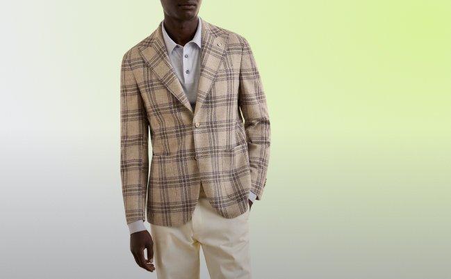 A man wearing a plaid Sport Jacket in a beige and brown check pattern, paired with a light gray collared shirt and cream trousers