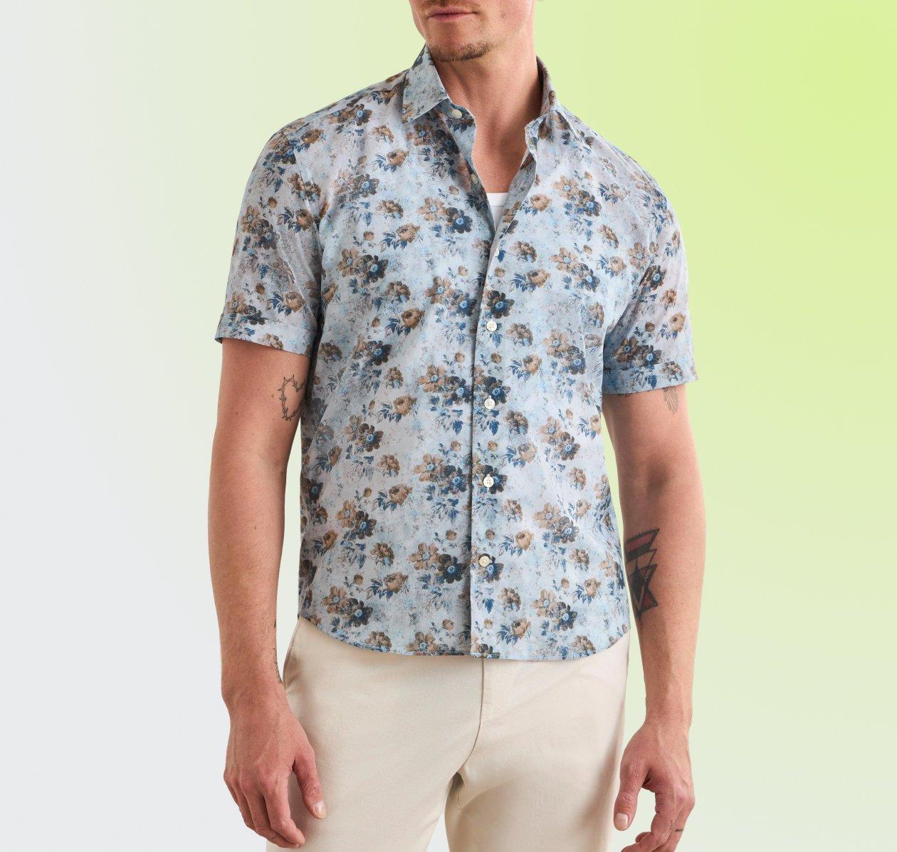 A man wearing a Floral Short Sleeve Button-Up Shirt in a light blue base with a tropical floral print