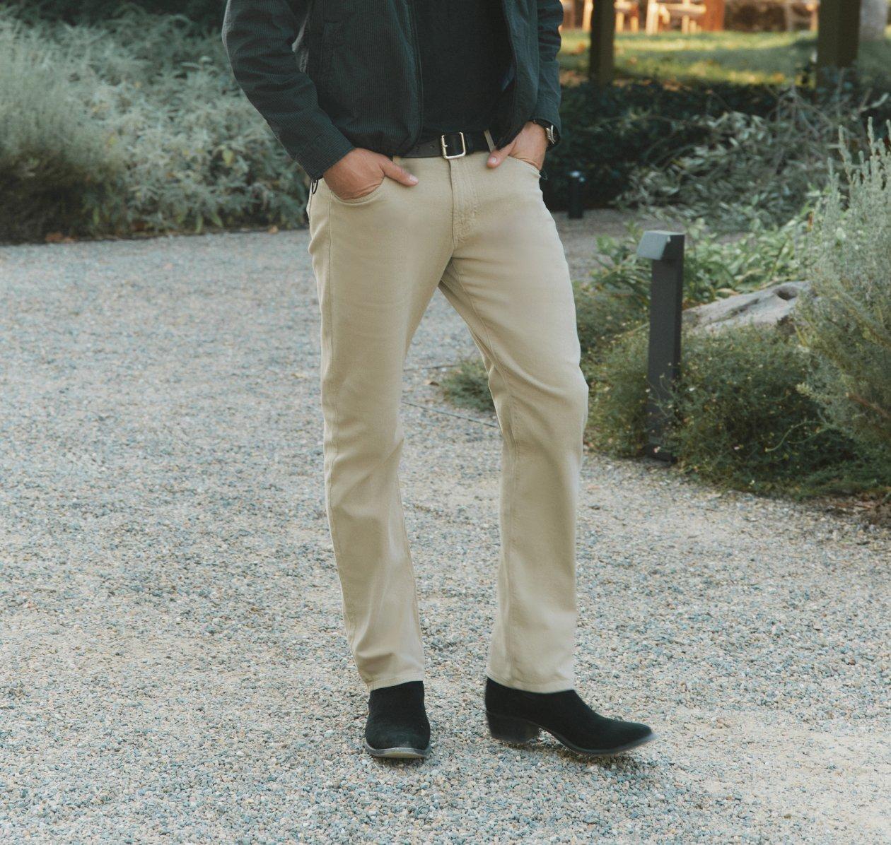Model wearing beige trousers, a dark jacket, and black suede ankle boots