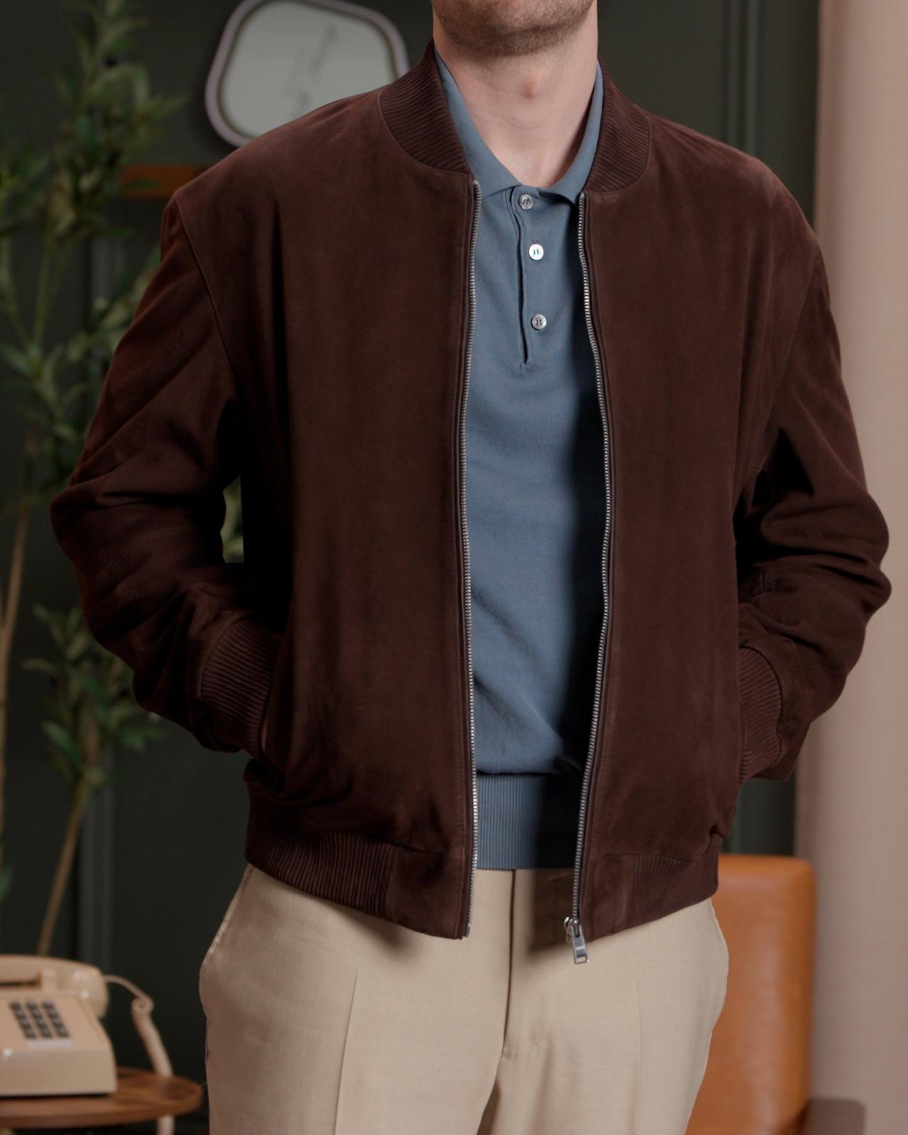 Closeup shot of fashion model wearing a dark brown suede jacket over a blue collared shirt, paired with beige trousers and dark brown shoes