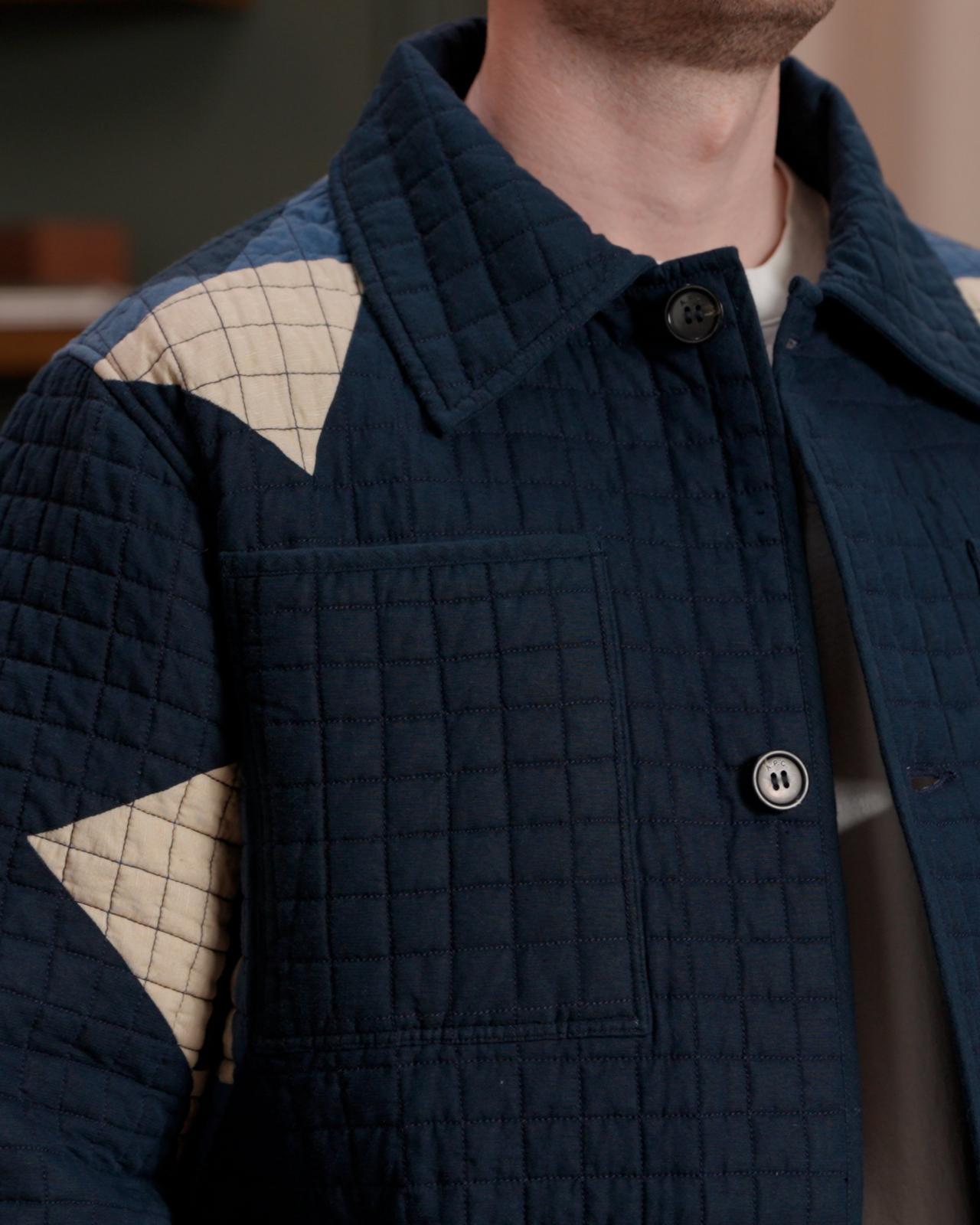 Plan rapproché d’un mannequin de mode portant une veste matelassée bleu marine avec des empiècements à motifs beiges, un t-shirt blanc uni, un jean bleu clair et des baskets blanches