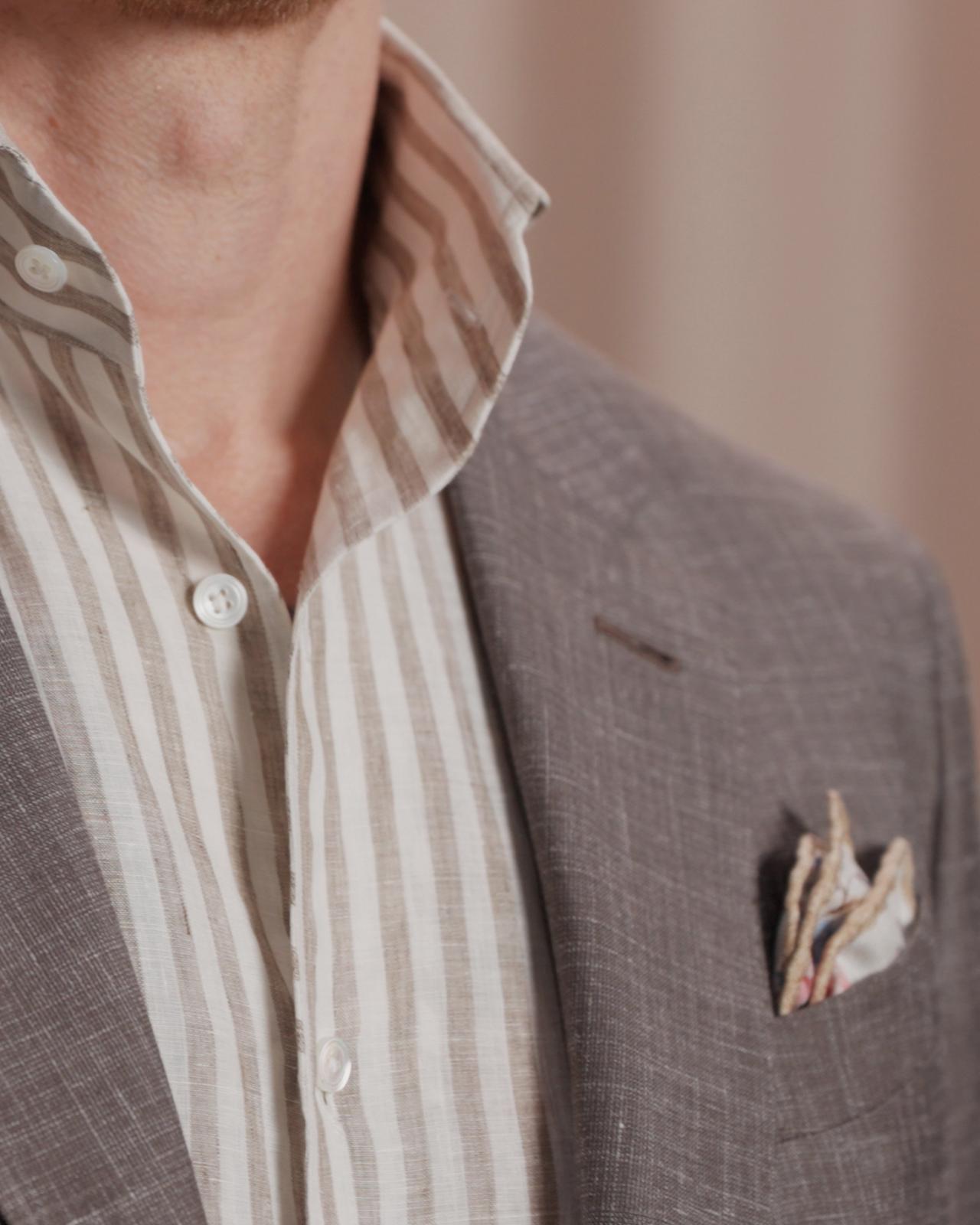 Un homme portant un manteau brun fumé, une chemise rayée blanc cassé et brun pâle avec une pochette
