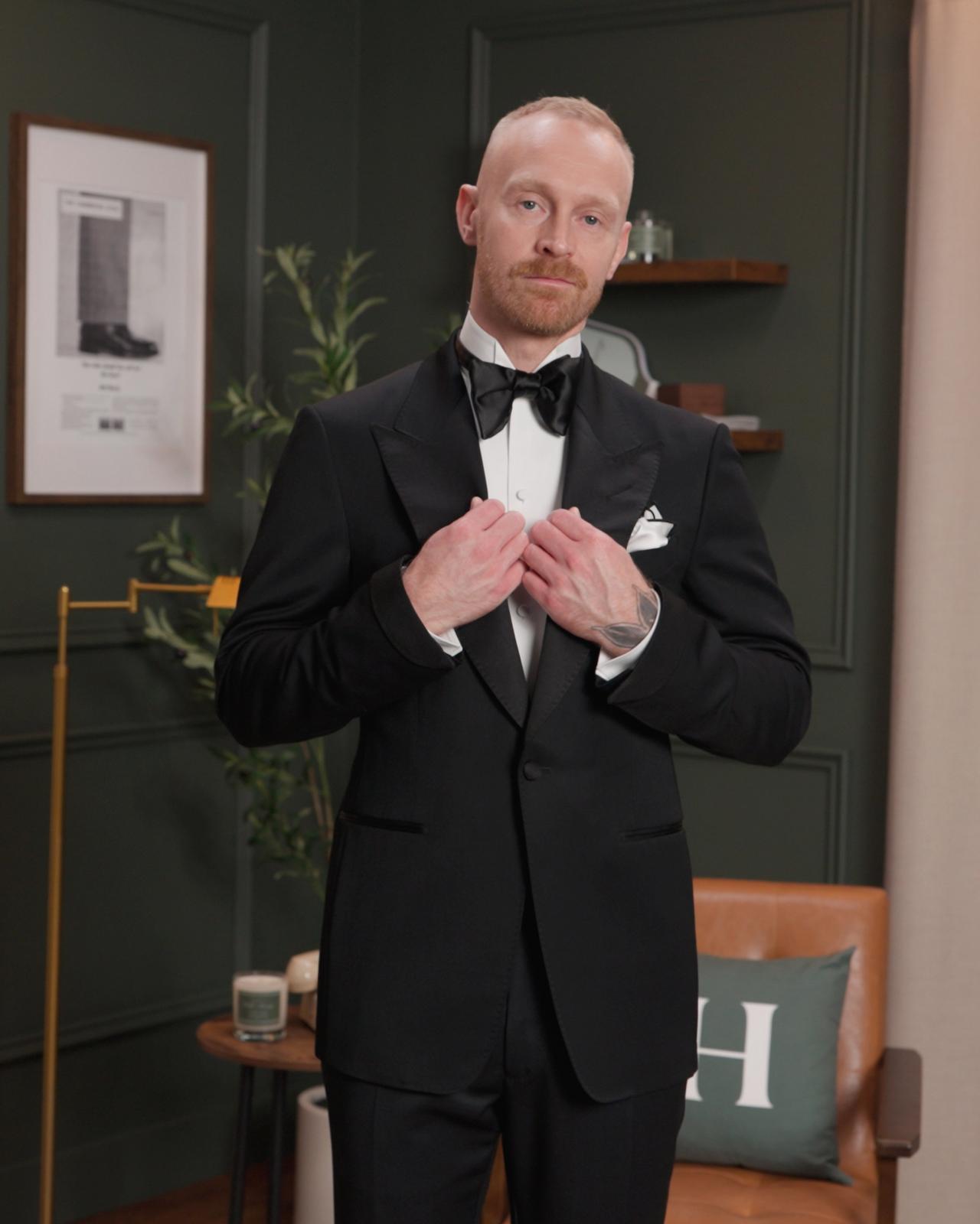 Un homme portant un nœud papillon noir avec un complet noir, une pochette blanche et noire et une chemise blanche