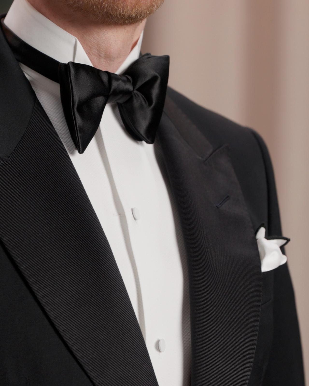 A close up of a black silk bow tie with white shirt