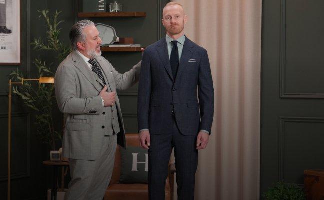 Un vendeur ajuste le costume d’un client essayant une veste bleu foncé, associée à une chemise bleu clair et une cravate somber