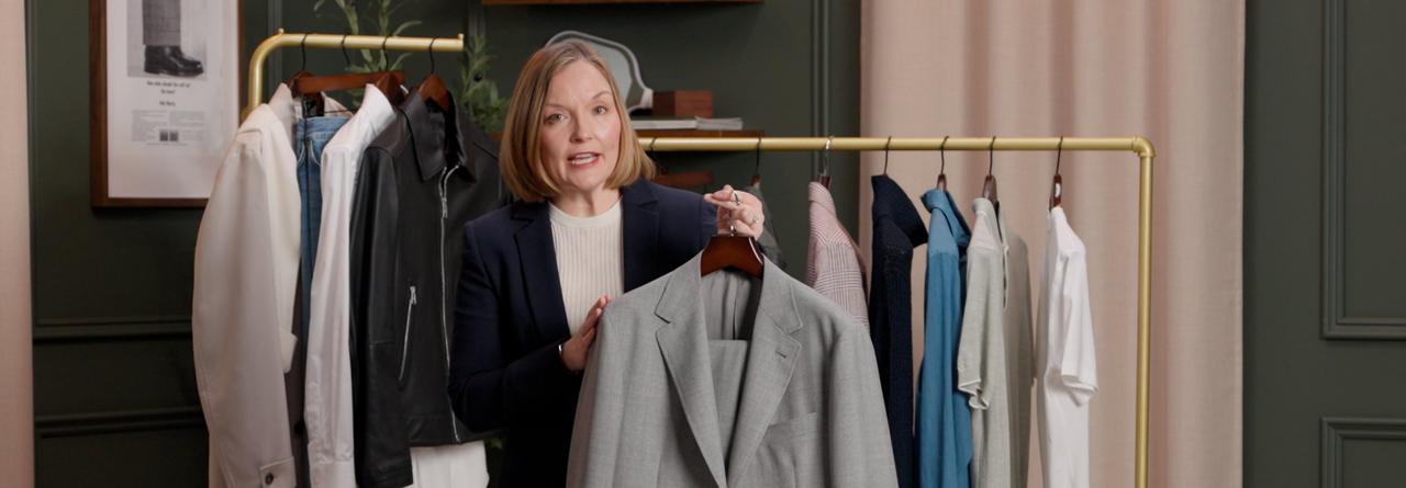 An associate holding a light gray suit jacket on a hanger