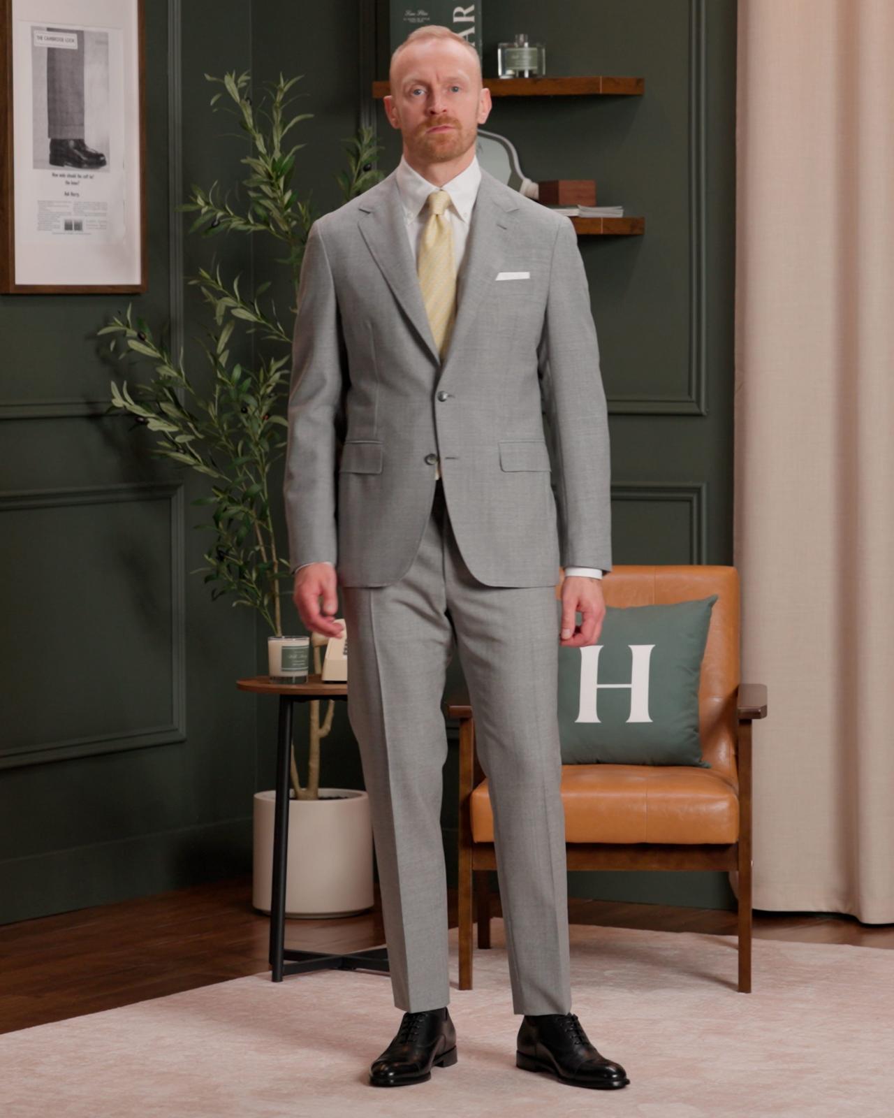 Fashion model wearing a light grey two-piece suit with a white dress shirt, a pale yellow tie, and black dress shoes