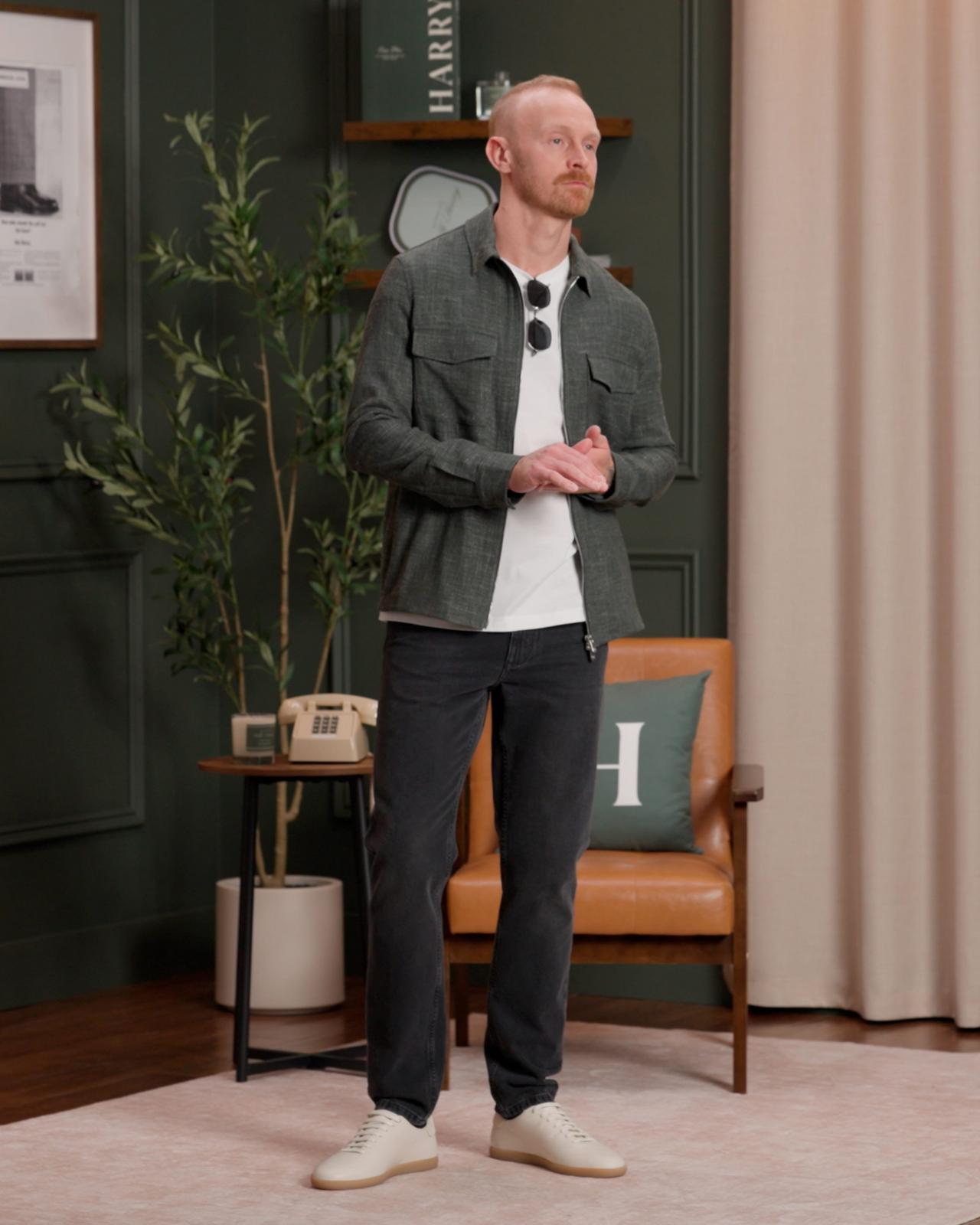 Fashion model wearing a dark green overshirt with front pockets over a white T-shirt, dark jeans, and white sneakers