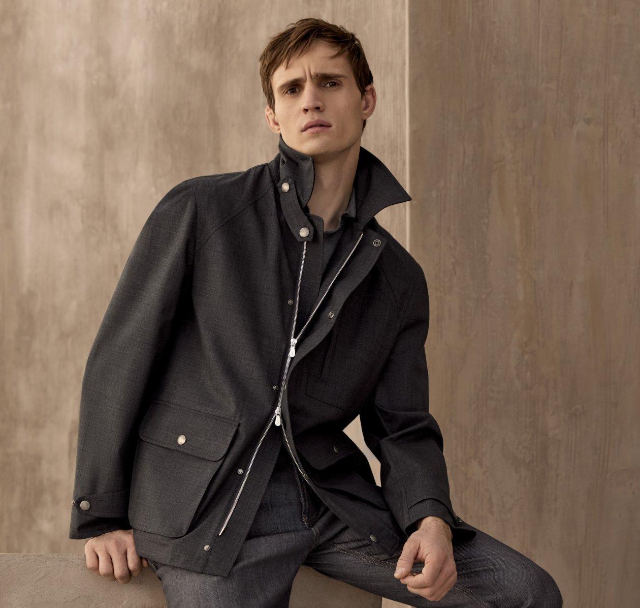 A model wearing a black water resistant Brunello Cucinelli jacket, styled with a knit polo, and black trousers