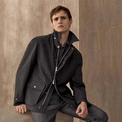 A model wearing a black water resistant Brunello Cucinelli jacket, styled with a knit polo, and black trousers
