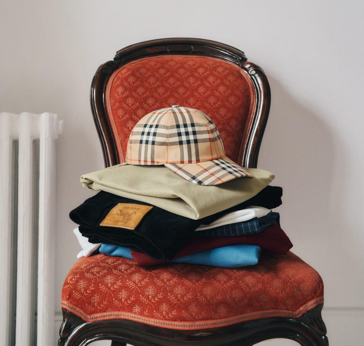 A tidy stack of Burberry clothing, carefully folded and finished with a beige plaid baseball cap on top