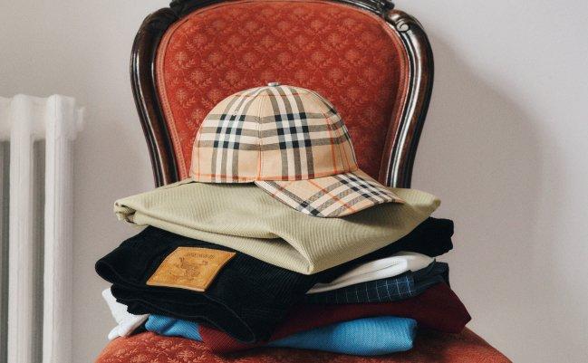 A tidy stack of Burberry clothing, carefully folded and finished with a beige plaid baseball cap on top