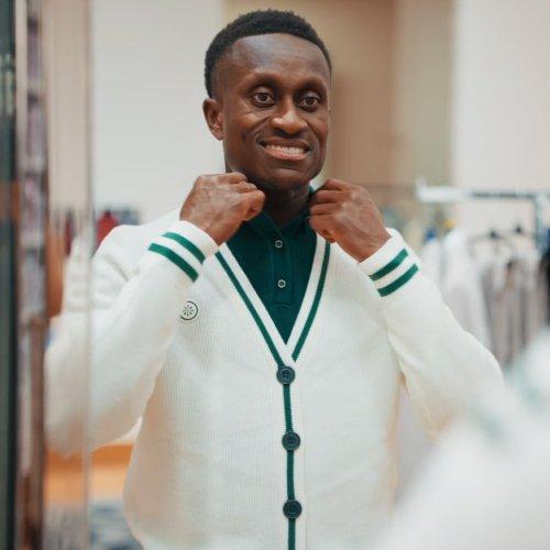 Canadian football player wearing a white cardigan with green trim and dark buttons is adjusting the collar of a dark green shirt underneath