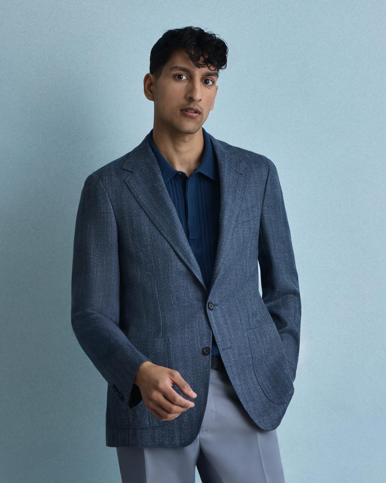 A model wearing a blue Canal sport jacket, navy blue knit polo, paired with slate grey dress pants