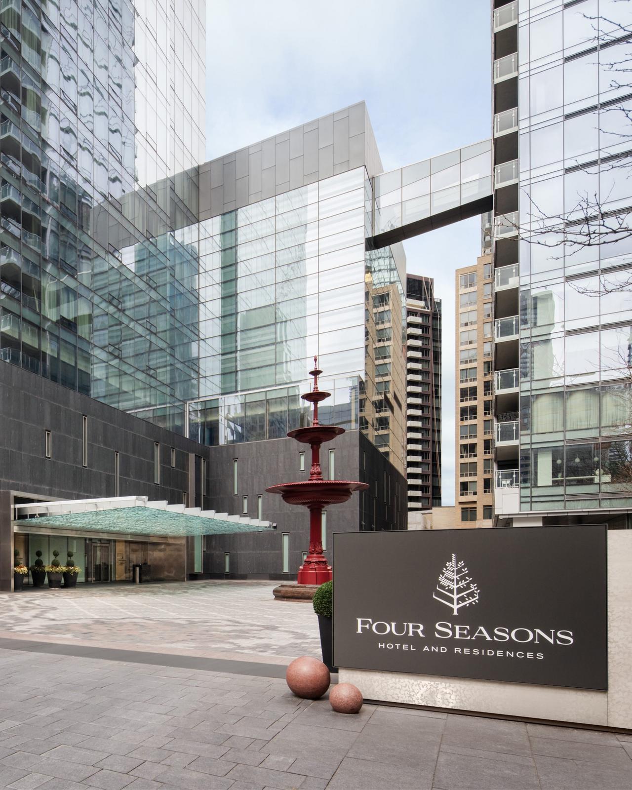 Four Seasons Hotel Toronto, featuring its modern glass façade, a striking red fountain, and a branded sign in the foreground