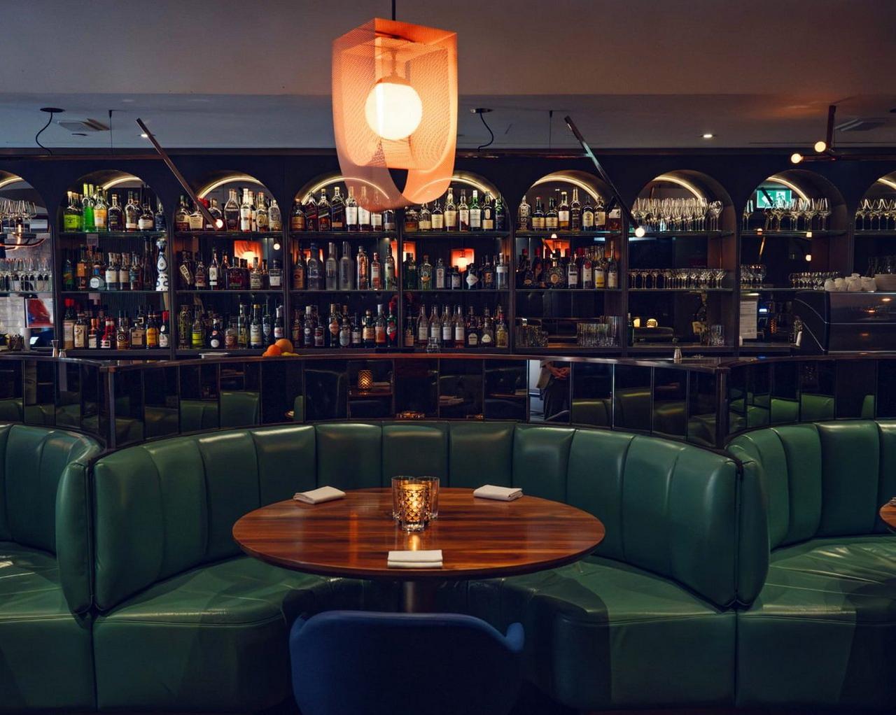 Alobar Yorkville, avec ses banquettes moelleuses en cuir vert, sa table en bois verni et un arrière-plan présentant une vaste sélection de bouteilles d’alcool