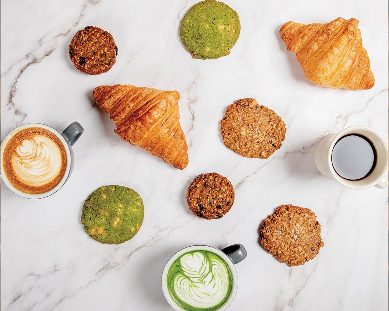 Des pâtisseries et des boissons, comprenant un croissant, des biscuits à l’avoine, un biscuit au matcha et deux tasses de café