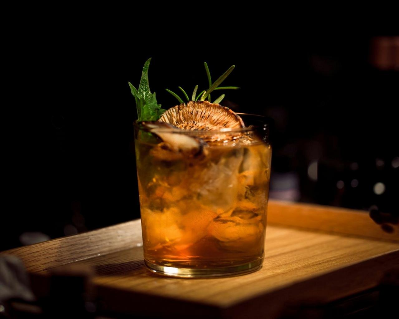 Un cocktail Moutai African Sunrise servi dans un verre à whisky, garni d’une tranche de fruit séché et d’herbes fraîches