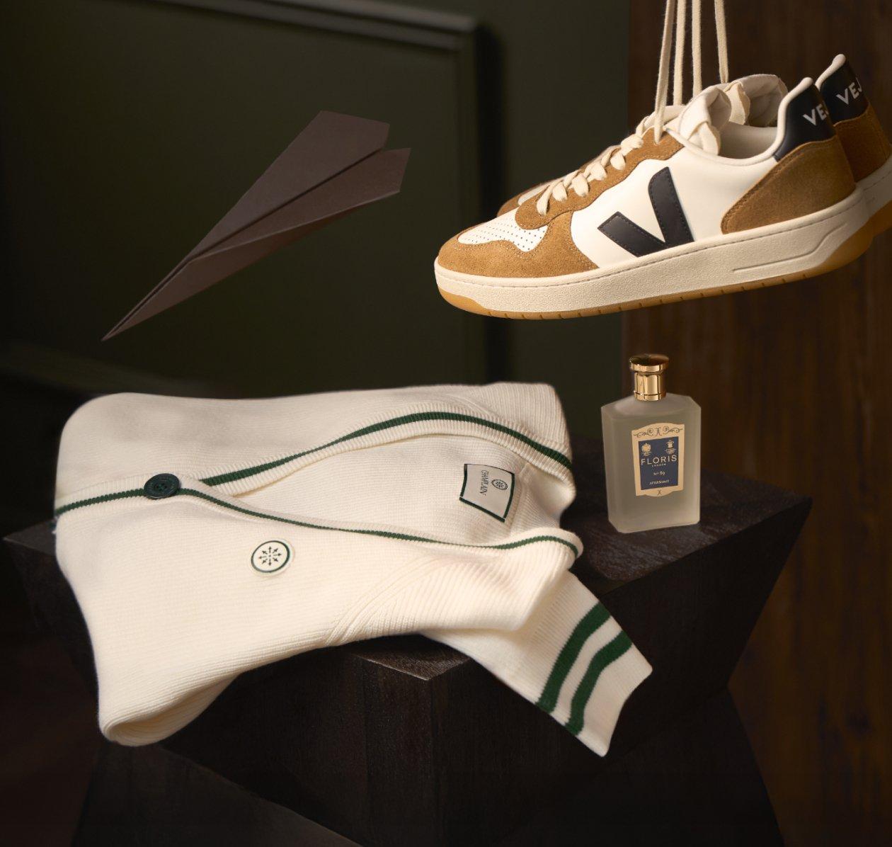 Image de mode présentant une paire de baskets dans un coloris blanc et marron, stylisées avec un cardigan en maille crème, un flacon de parfum et une cravate bleue