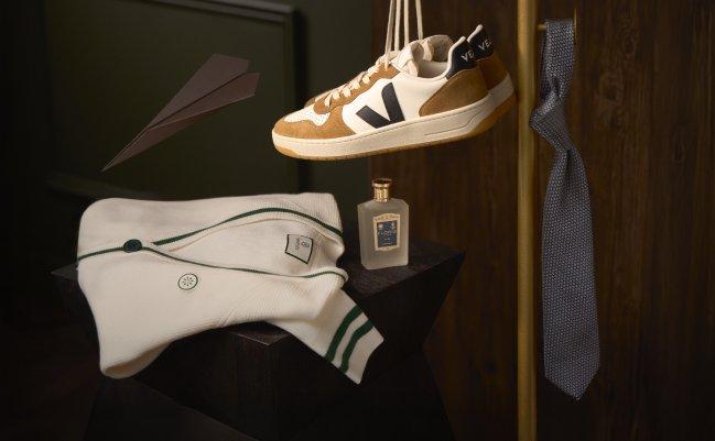 Fashion image featuring a pair of sneakers in a white and brown colorway, styled alongside a cream knit cardigan, a bottle of perfume and blue tie