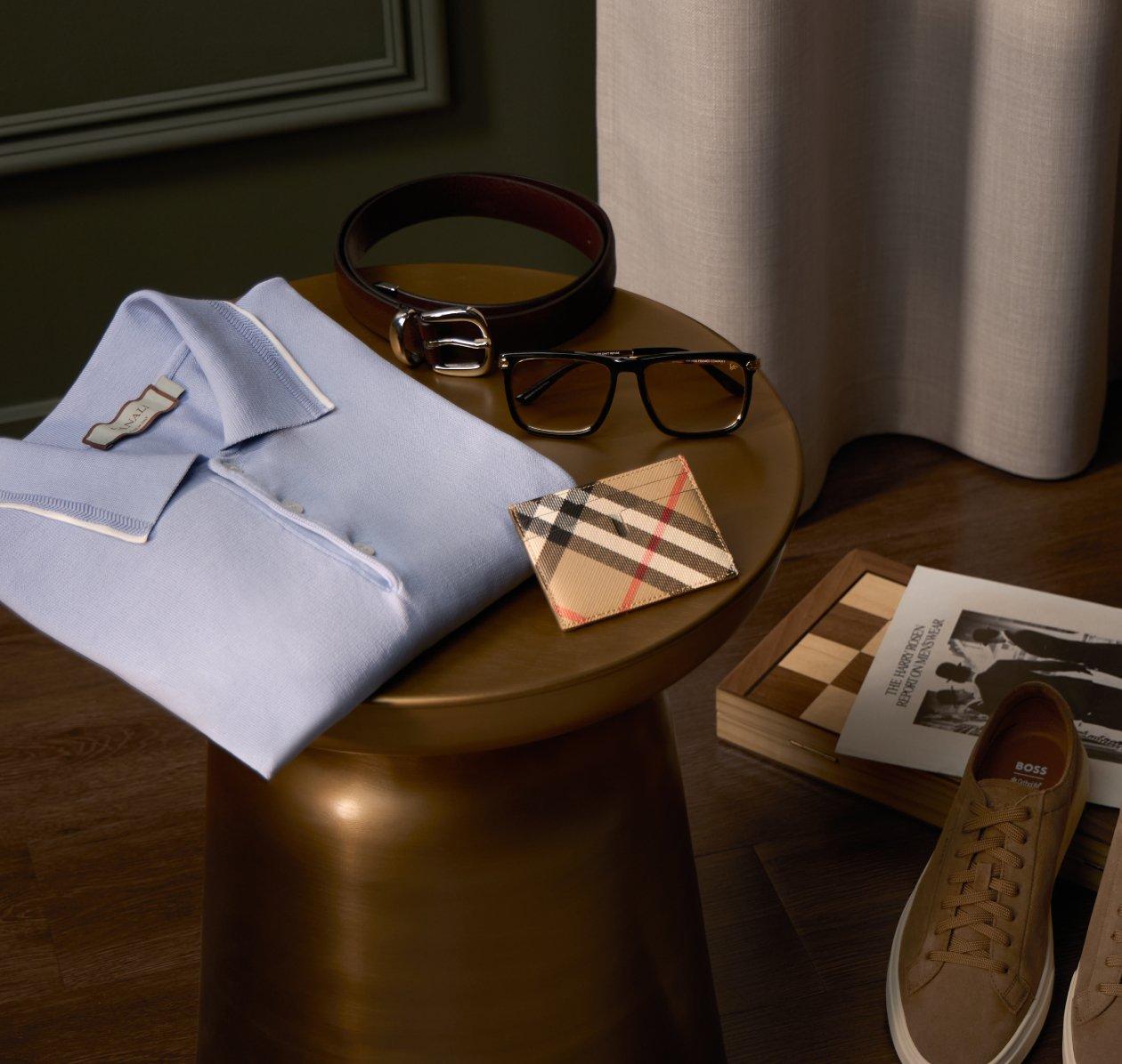 accesorios para hombre, incluyendo una camisa celeste con cuello, un cinturón de cuero, gafas, una billetera con estampado y un par de zapatos