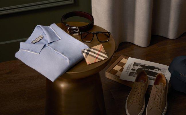 men's accessories, including a light blue collared shirt, a leather belt, eyeglasses, a patterned wallet, and a pair of shoes